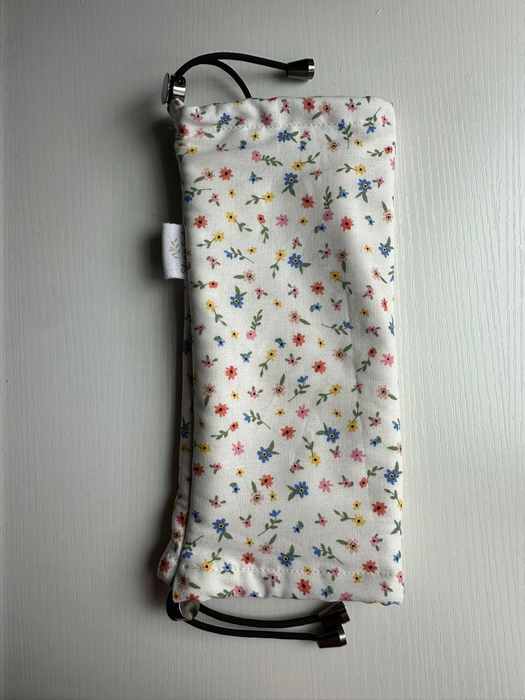 Sling Safe drawstring washing cover for ring slings, shown in the pattern Confetti. Confetti is a pattern with blue, red, yellow and pink flowers throughought a white background.