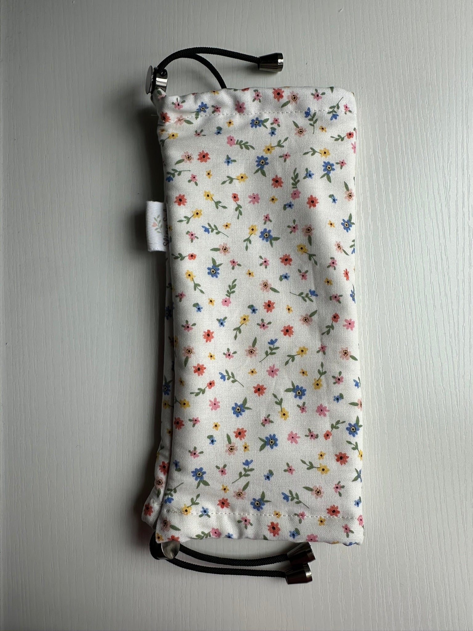 Sling Safe drawstring washing cover for ring slings, shown in the pattern Confetti. Confetti is a pattern with blue, red, yellow and pink flowers throughought a white background.