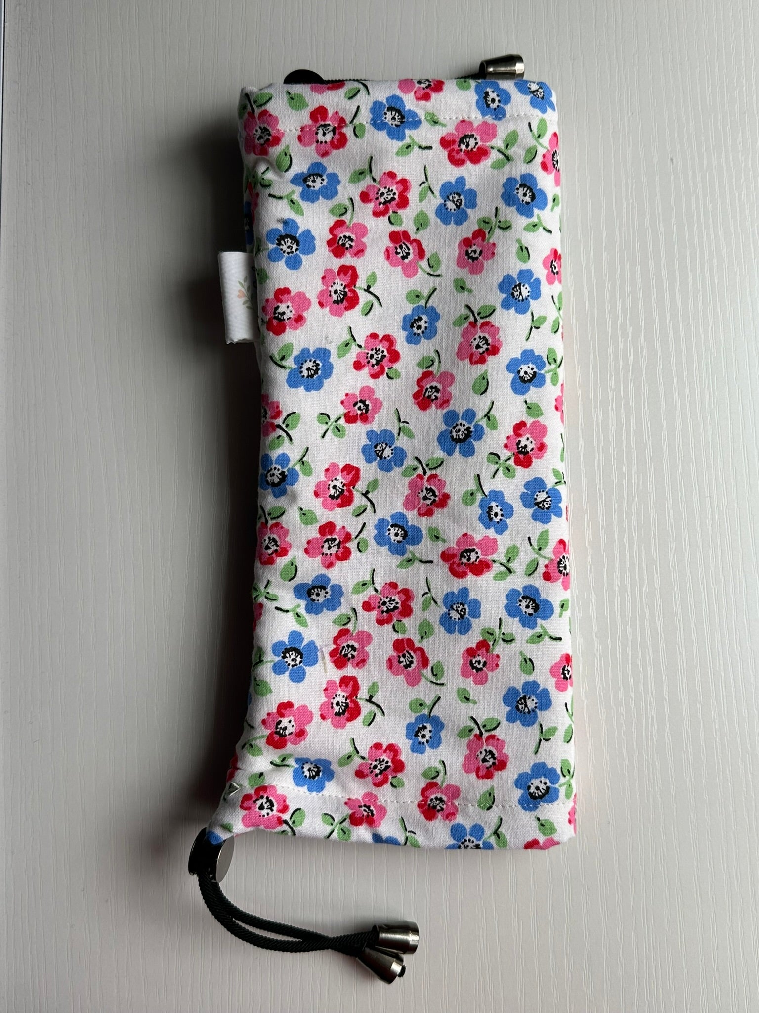 Sling Safe drawstring washing cover for ring slings, shown in the pattern Cottage Posy. Cottage Posy is a dark pink and blue floral with a white background. 