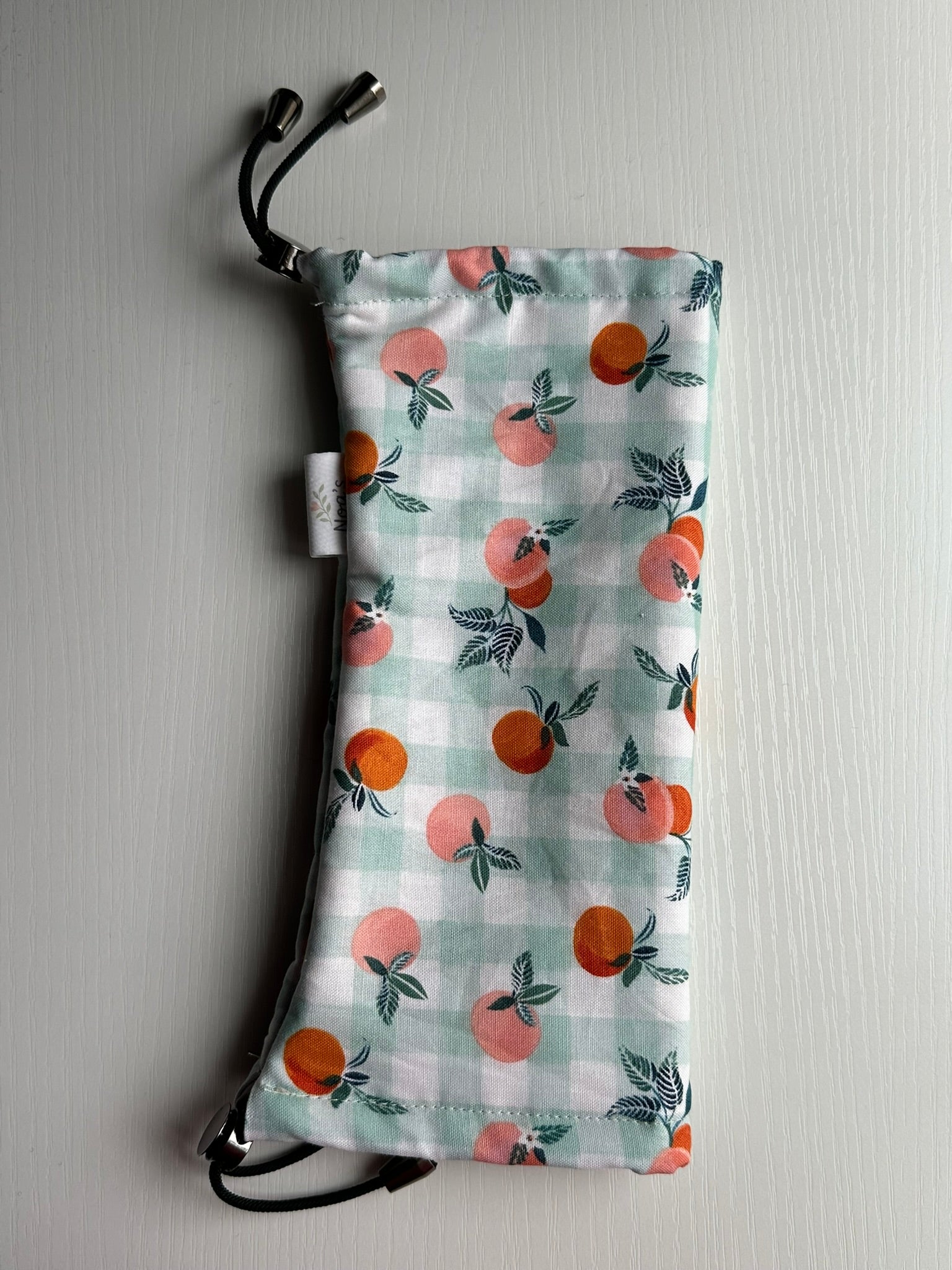 Sling Safe drawstring washing cover for ring slings, shown in the pattern Georgia. Georgia is a teal and white gingham with peaches throughout