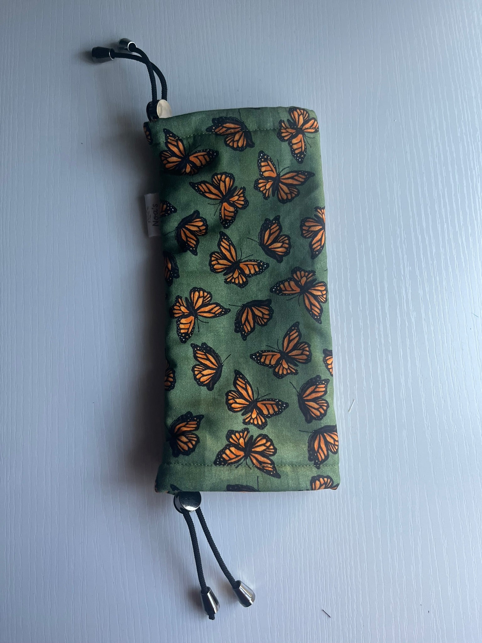 Sling Safe drawstring washing cover for ring slings, shown in the pattern Monarch. Monarch is a green background with orange monarch butterflies throughout. 