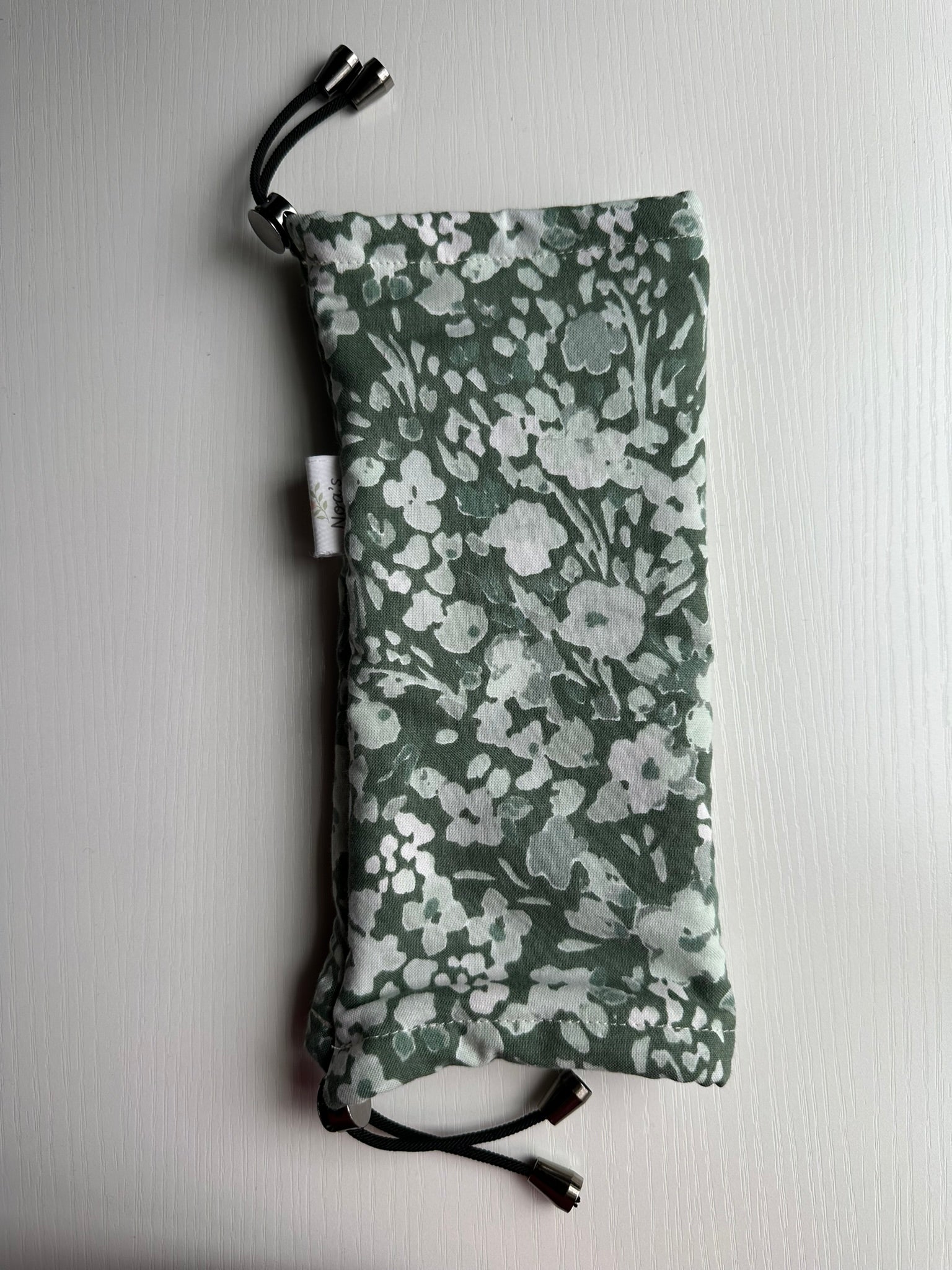 Sling Safe drawstring washing cover for ring slings, shown in Olive Meadow fabric. Olive Meadow is a forest green background with various lighter green flowers and leaves.