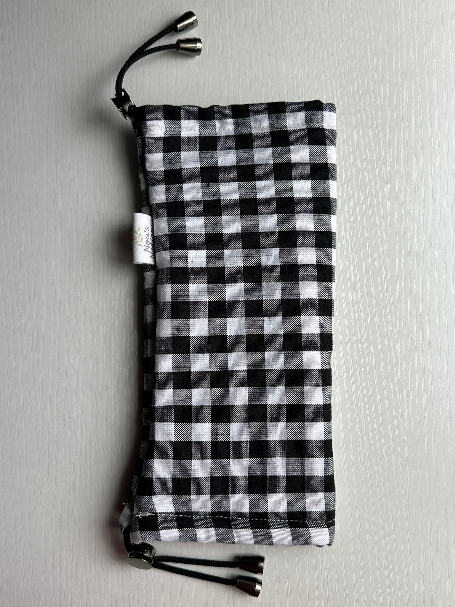 Sling Safe drawstring washing cover for ring slings, shown in "Salt" fabric. Salt is a black and white gingham fabric.