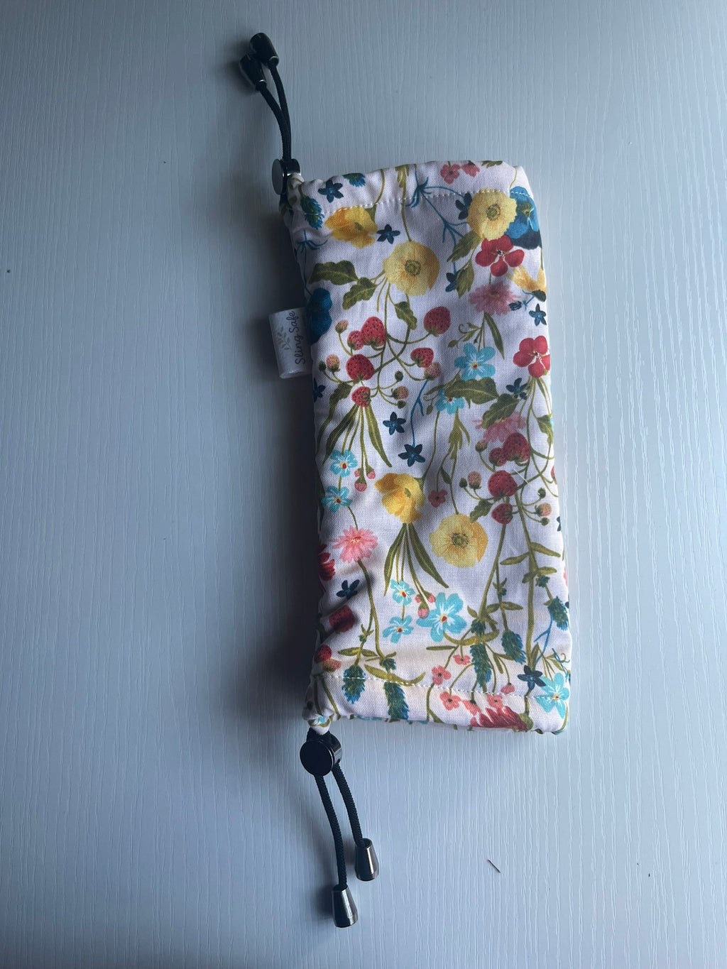 Sling Safe drawstring washing cover for ring slings, shown in the pattern Wildflower. Wildflower is a beige background with multiple flowers and strawberries throughout. 